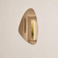 Organische spiegel model 2 in brons spiegelglas aan een licht beige muur met fijne structuur.