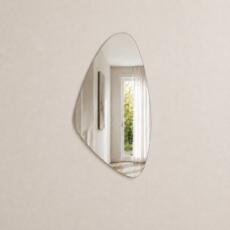 Organische spiegel model 2 in verzilverd spiegelglas aan een licht beige muur met fijne structuur.