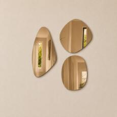 Organische spiegelset van drie bronzen spiegels in verschillende vormen op een beige wand.