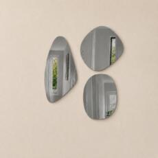 Organische spiegelset van drie grijs getinte spiegels in verschillende vormen op een beige wand.