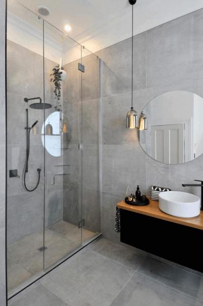 Badkamer met een glazen douchedeur en ronde spiegel